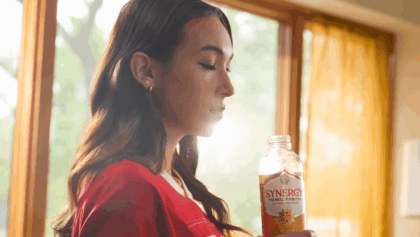 Young woman sipping SYNERGY kombucha in front of sunlit window