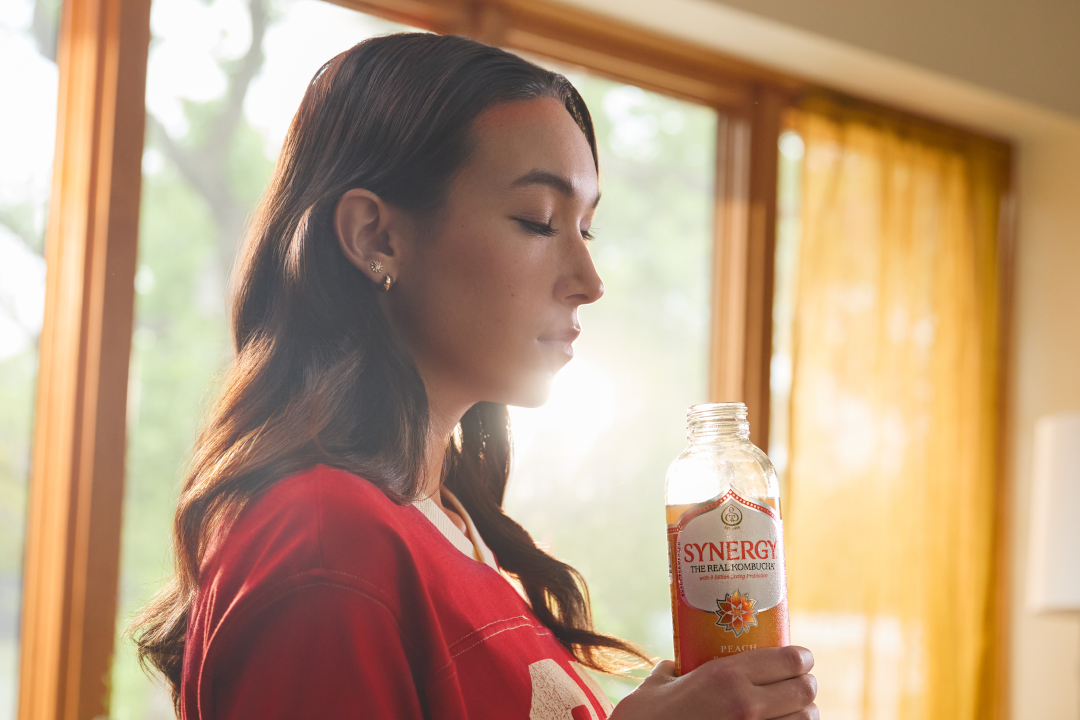 Young woman sipping SYNERGY kombucha in front of sunlit window